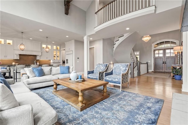living area with a towering ceiling, stairway, light wood-style flooring, baseboards, and decorative columns