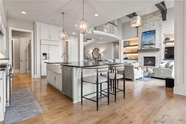 kitchen with a sink, dishwasher, a kitchen bar, a stone fireplace, and white cabinets