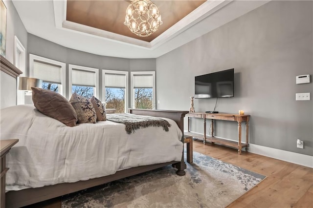 bedroom featuring a raised ceiling, a chandelier, wood finished floors, and baseboards