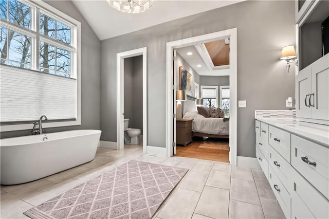 full bathroom with tile patterned flooring, a freestanding tub, toilet, lofted ceiling, and baseboards