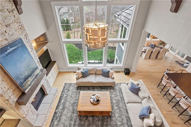 living room with a glass covered fireplace, a high ceiling, wood finished floors, a chandelier, and baseboards