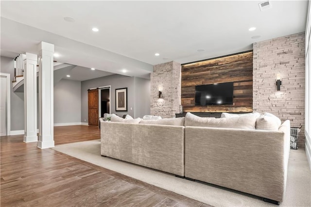 living room featuring an accent wall, ornate columns, baseboards, recessed lighting, and wood finished floors
