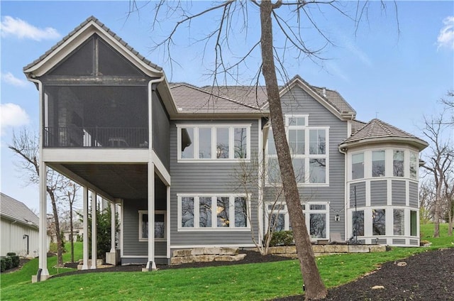 back of house featuring a sunroom, a lawn, and a tile roof