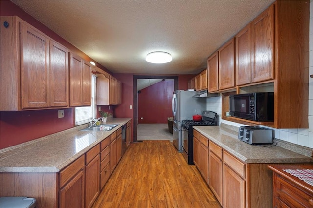 kitchen with brown cabinetry, a textured ceiling, a sink, light wood finished floors, and black appliances