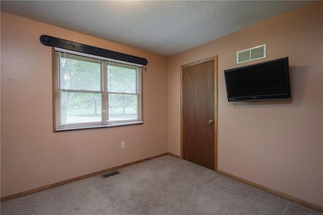 spare room with visible vents, a textured ceiling, carpet floors, and baseboards