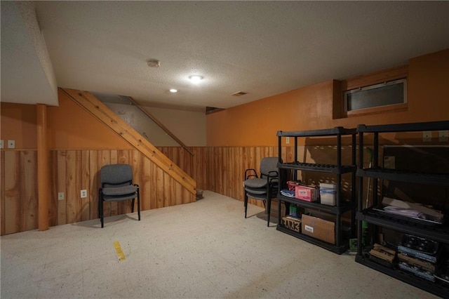 finished basement with a textured ceiling, tile patterned floors, wood walls, a wainscoted wall, and stairs