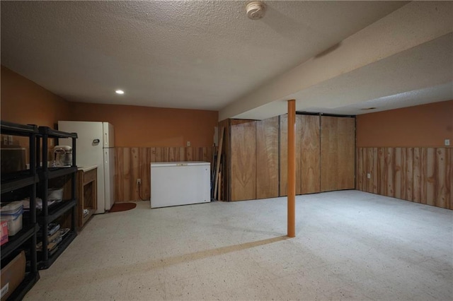 finished below grade area featuring freestanding refrigerator, wood walls, refrigerator, light floors, and a textured ceiling