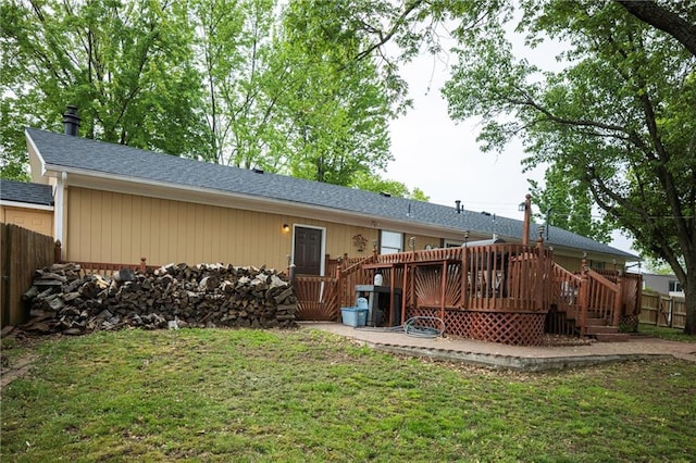 rear view of house featuring a lawn, a shingled roof, fence, and a wooden deck