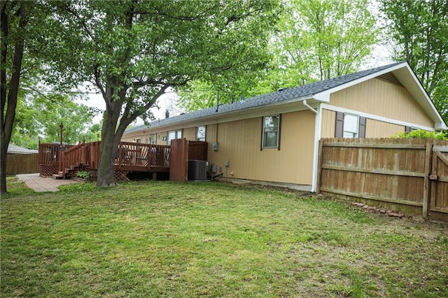 back of property with fence, a wooden deck, roof with shingles, a lawn, and central air condition unit