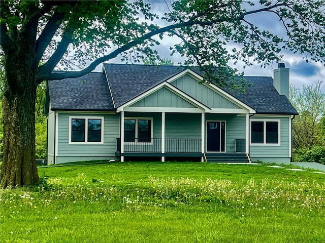 view of front of house with a front lawn, roof with shingles, a chimney, board and batten siding, and a porch
