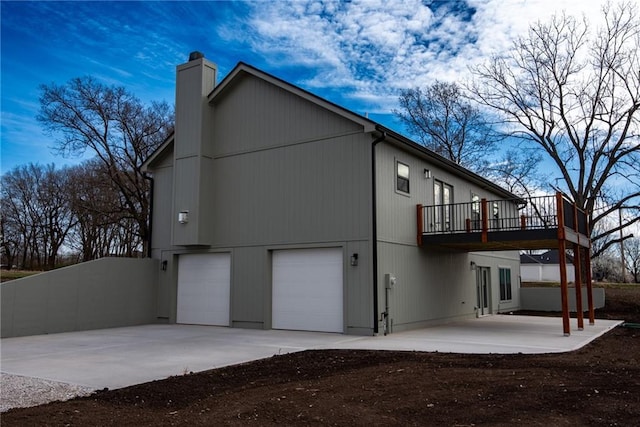 back of property with a wooden deck, a chimney, a patio area, concrete driveway, and an attached garage