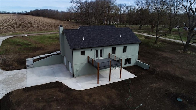 back of property featuring a rural view, driveway, a chimney, and a shingled roof