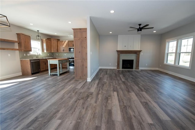 unfurnished living room with baseboards, a ceiling fan, plenty of natural light, and dark wood-type flooring