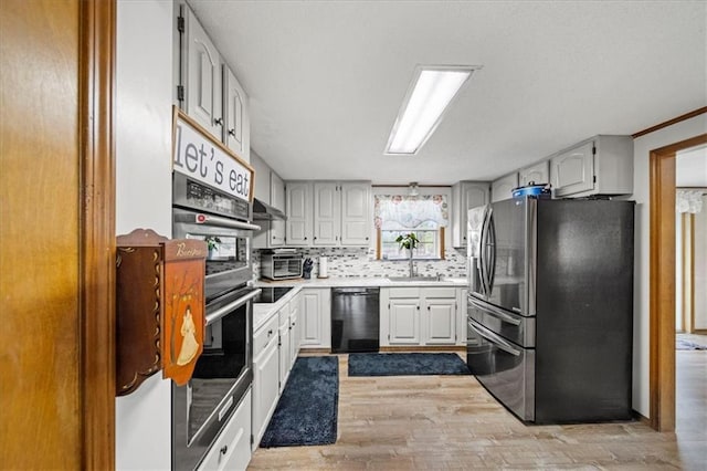 kitchen with light countertops, a sink, light wood-style floors, black appliances, and backsplash