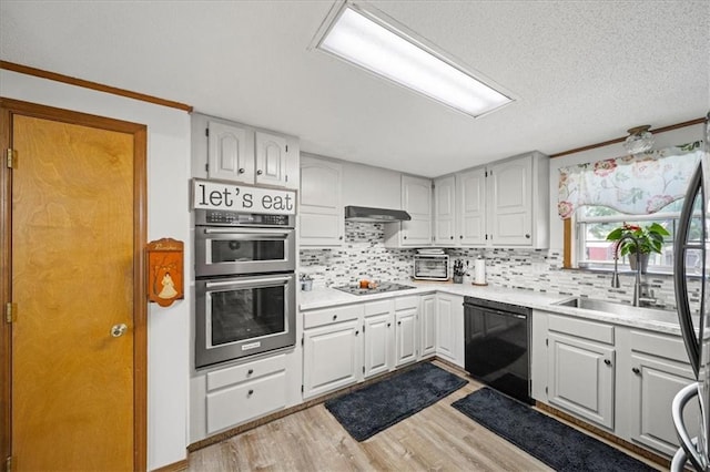 kitchen featuring wood finished floors, black dishwasher, under cabinet range hood, a sink, and double oven