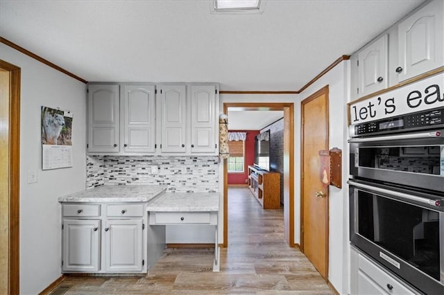 kitchen featuring double oven, tasteful backsplash, light wood-style floors, and ornamental molding