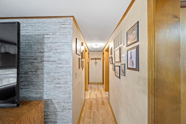 hall featuring light wood-style floors, wood walls, and a textured ceiling