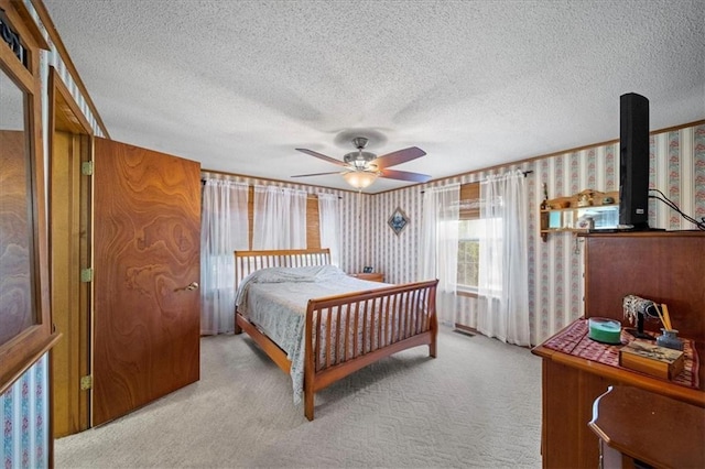 bedroom featuring a textured ceiling, wallpapered walls, a ceiling fan, light carpet, and a wood stove