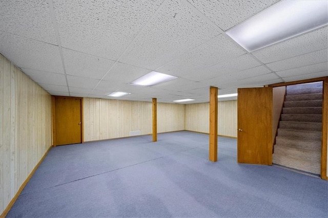 finished basement with carpet floors, wood walls, a paneled ceiling, and stairway