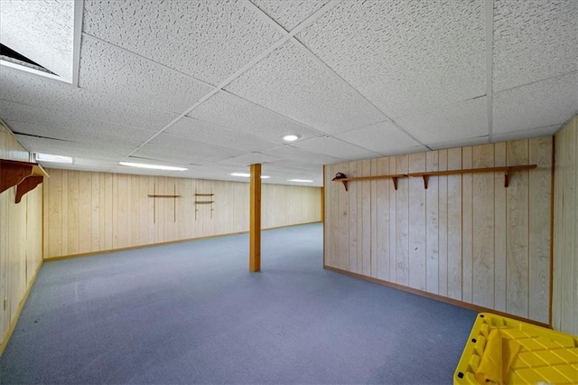 finished below grade area featuring baseboards, carpet floors, wood walls, and a paneled ceiling