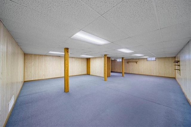 finished basement featuring visible vents, wooden walls, and a paneled ceiling