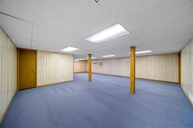 finished below grade area featuring baseboards, carpet floors, wood walls, and a paneled ceiling