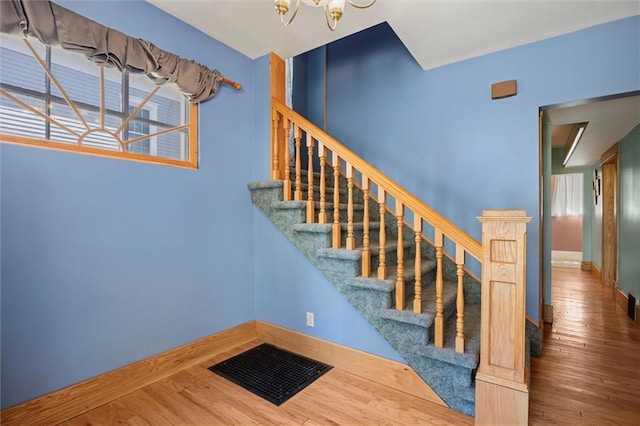 stairway featuring baseboards, a notable chandelier, wood finished floors, and a healthy amount of sunlight