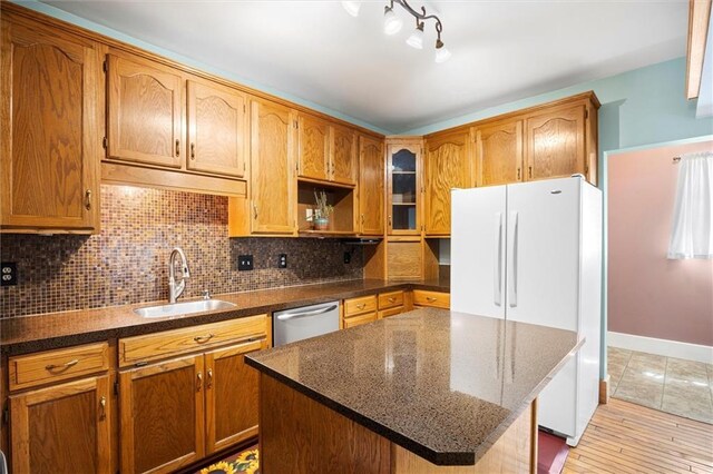 kitchen with tasteful backsplash, dark stone countertops, freestanding refrigerator, stainless steel dishwasher, and a sink