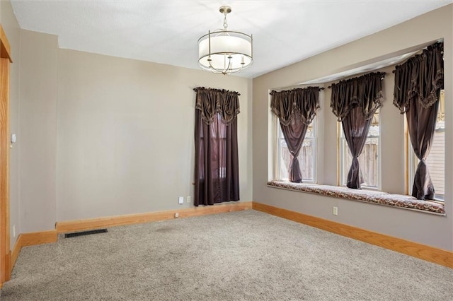 carpeted empty room featuring a chandelier, visible vents, and baseboards
