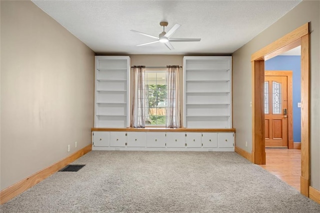 empty room with visible vents, a textured ceiling, light colored carpet, and ceiling fan