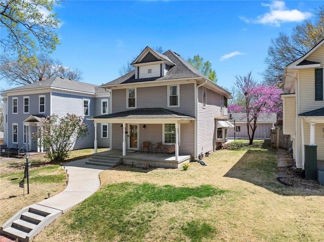 american foursquare style home featuring roof with shingles, fence, and a front lawn