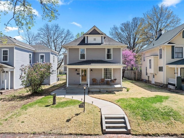 traditional style home featuring a front yard, fence, covered porch, and roof with shingles