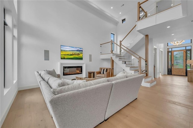 living room featuring a high ceiling, a glass covered fireplace, light wood-type flooring, stairs, and baseboards