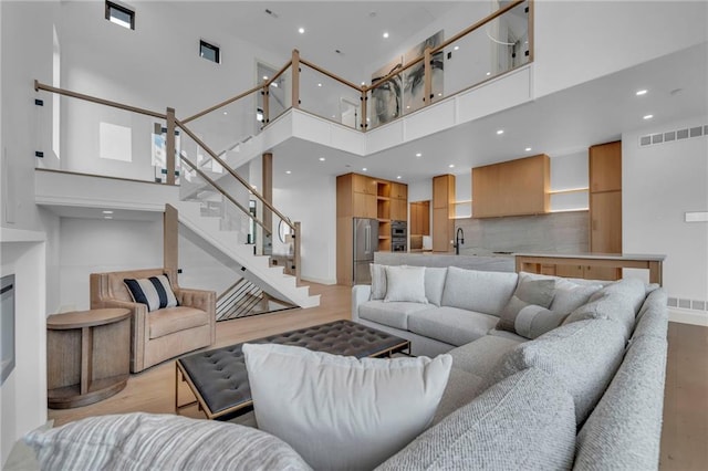 living area featuring a towering ceiling, light wood finished floors, visible vents, and recessed lighting