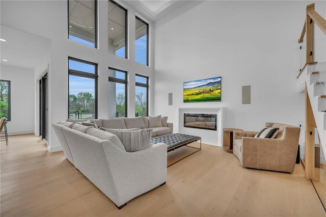 living area featuring recessed lighting, wood finished floors, a towering ceiling, and a glass covered fireplace