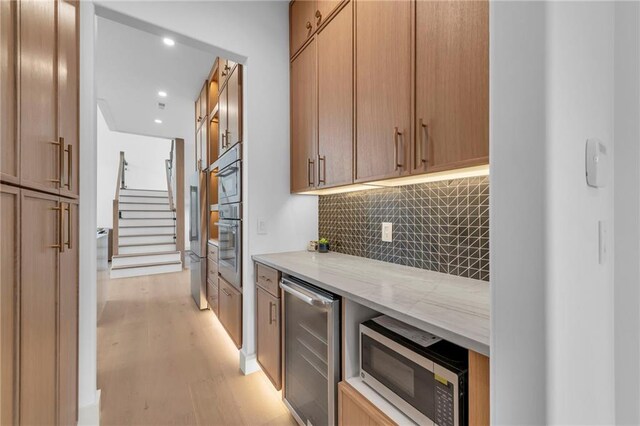 bar featuring stainless steel microwave, decorative backsplash, light wood-style flooring, beverage cooler, and recessed lighting