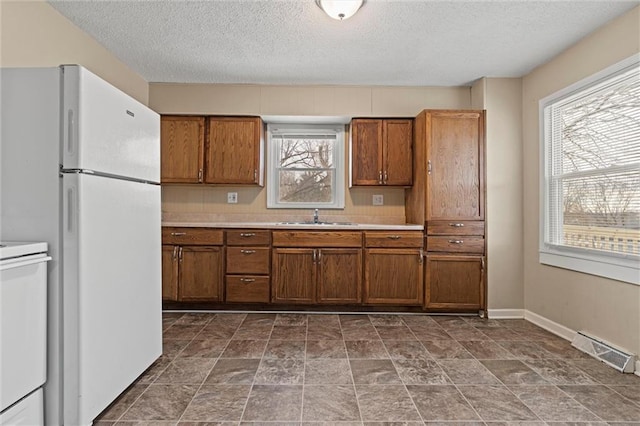 2701 Wilson Ave, Leavenworth, KS 66048 - kitchen featuring freestanding refrigerator, a sink, brown cabinetry, light countertops, and a textured ceiling