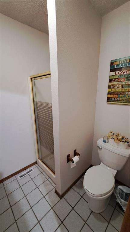 2101A Dove Rd, Longton, KS 67352 - full bath featuring toilet, a shower stall, a textured ceiling, tile patterned floors, and visible vents