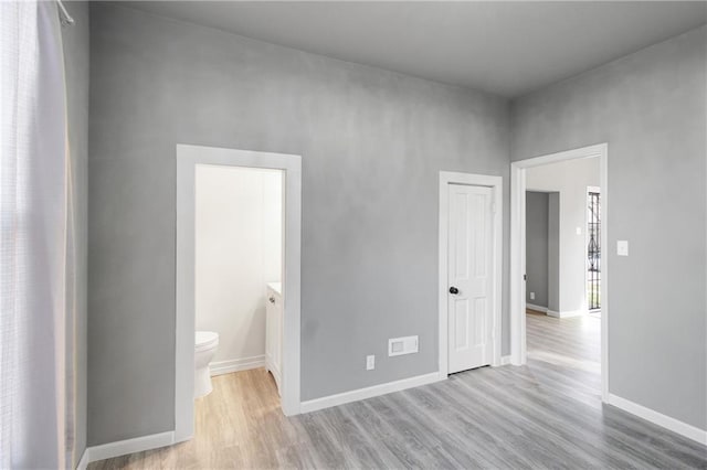 unfurnished bedroom with connected bathroom, baseboards, and wood finished floors