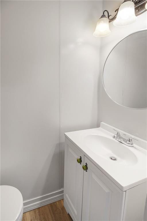 half bath with toilet, vanity, baseboards, and wood finished floors