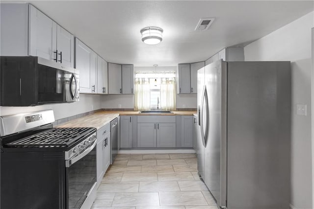 kitchen featuring gray cabinets, stainless steel appliances, a sink, wood counters, and visible vents