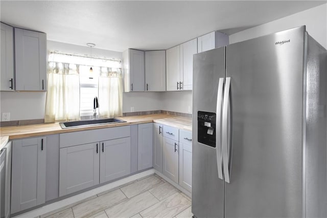 kitchen with butcher block countertops, stainless steel appliances, a sink, decorative light fixtures, and gray cabinets
