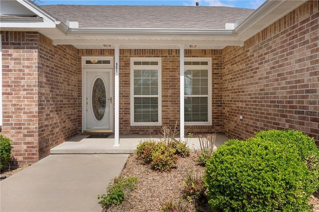 entrance to property featuring brick siding and a shingled roof