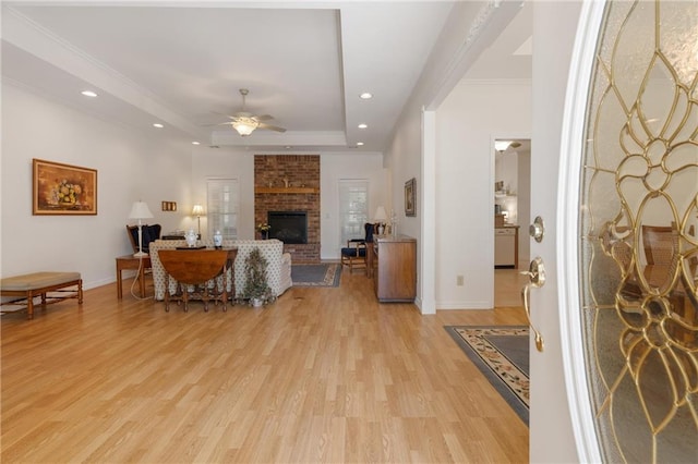 living area featuring a ceiling fan, light wood-type flooring, a tray ceiling, a fireplace, and baseboards