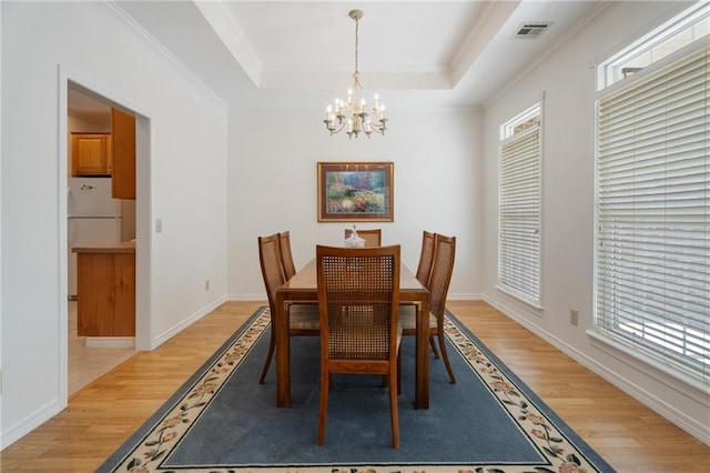 dining space with light wood-style flooring, a tray ceiling, visible vents, a notable chandelier, and crown molding