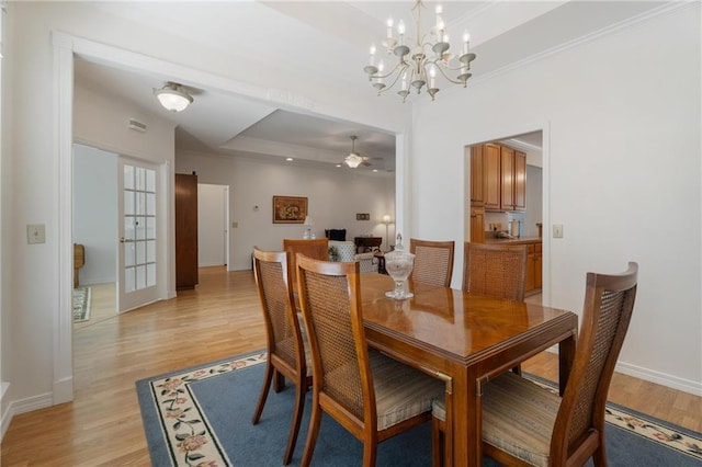 dining area featuring light wood-type flooring, baseboards, a raised ceiling, and ceiling fan with notable chandelier