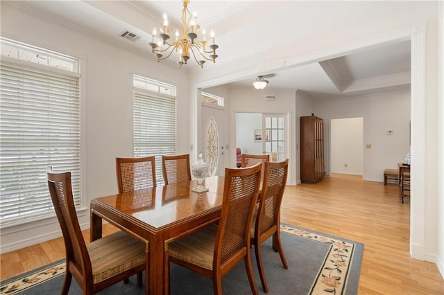 dining area with light wood-style flooring, an inviting chandelier, a raised ceiling, ornamental molding, and visible vents