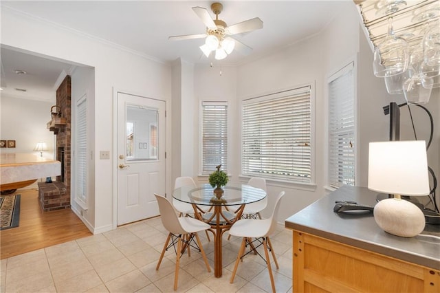 dining space featuring a brick fireplace, ornamental molding, ceiling fan, and light tile patterned floors