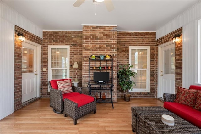 living area with wood finished floors, ornamental molding, ceiling fan, and brick wall