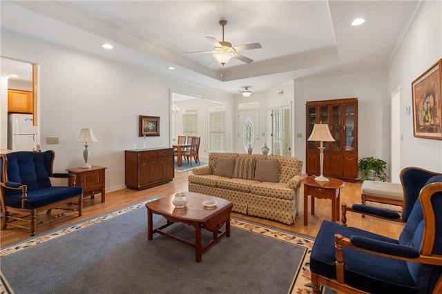 living room featuring a ceiling fan, crown molding, a tray ceiling, light wood finished floors, and recessed lighting